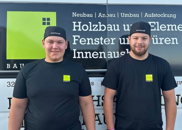 Zwei Handwerker vor Firmenfahrzeug mit Schriftzug für Holzbau, Fenster, Türen und Innenausbau, tragen Firmenkleidung.