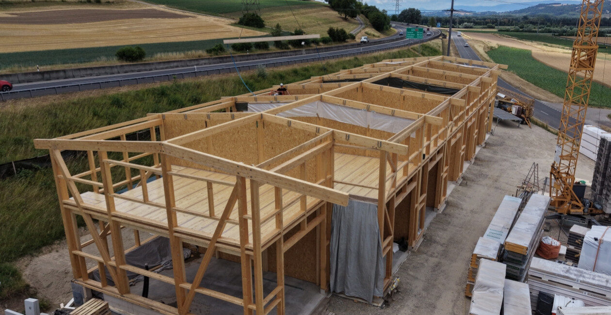 Holzrahmenbau eines Gebäudes neben einer Landstraße unter blauem Himmel mit Wolken im Hintergrund.