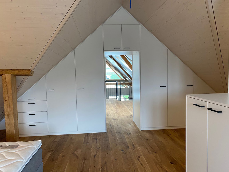 Modernes Dachgeschoss mit Einbauschränken, Holzfußboden und großem Fenster für viel natürliches Licht.