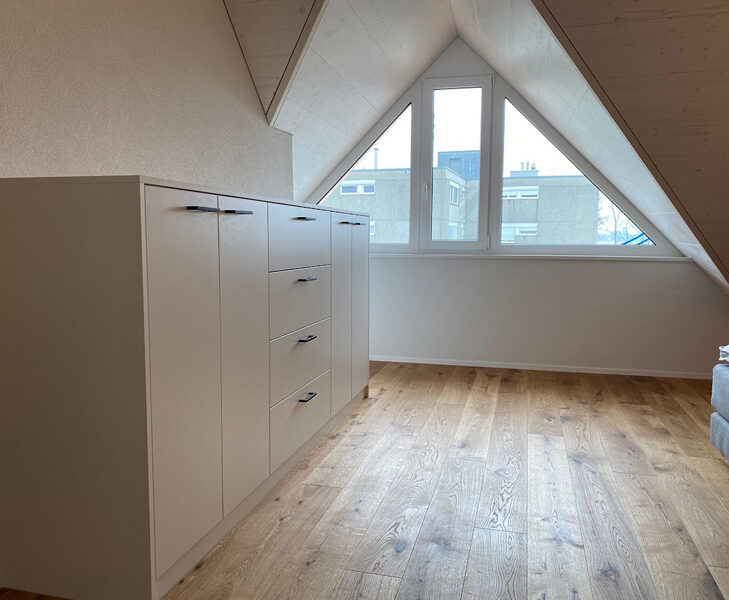 Modernes Dachgeschosszimmer mit Holzfußboden, weißem Einbauschrank und großem Fenster für viel Tageslicht.