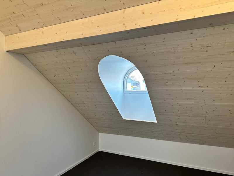 Holzverkleidete Dachschräge mit halbrundem Fenster und Tageslichteinfall im modernen Innenraum.