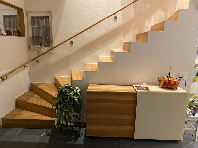 Moderne Holztreppe mit Pflanze und Deko auf Kommode vor weißer Wand in einem stilvollen Innenraum.