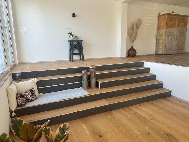 Moderne, minimalistische Wohnzimmertreppe aus Holz mit Deko-Elementen und Kissen für gemütliches Ambiente.