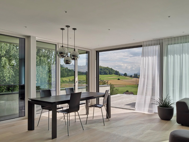 Modernes Esszimmer mit großen Fenstern und Blick auf die idyllische Landschaft. Minimalistische Einrichtung und Hängelampen.