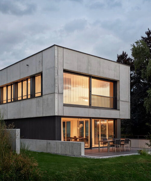 Modernes zweistöckiges Haus aus Beton mit großen Fenstern und Garten bei Sonnenuntergang.