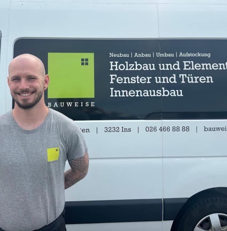 Lächelnder Mann vor Bauweise-Transporter mit Beschriftung für Holzbau und Innenausbau-Dienstleistungen.